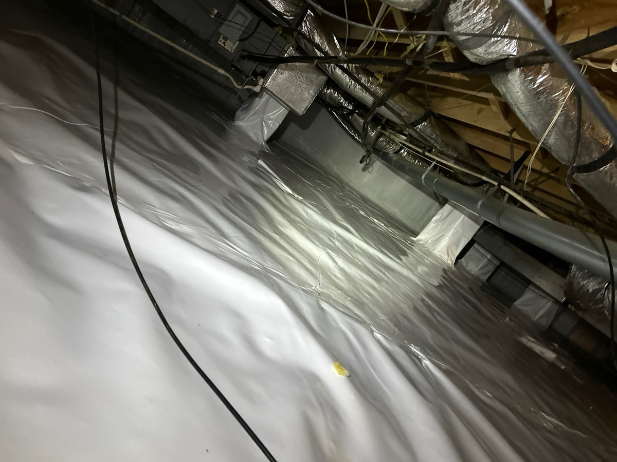 White vapor barrier being installed along crawl space walls during encapsulation
