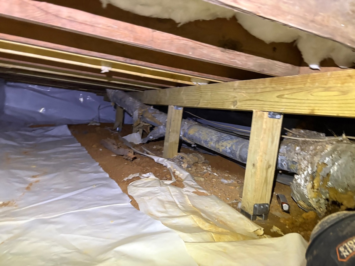 Rotted floor joist with exposed plumbing — before foundation reinforcement
