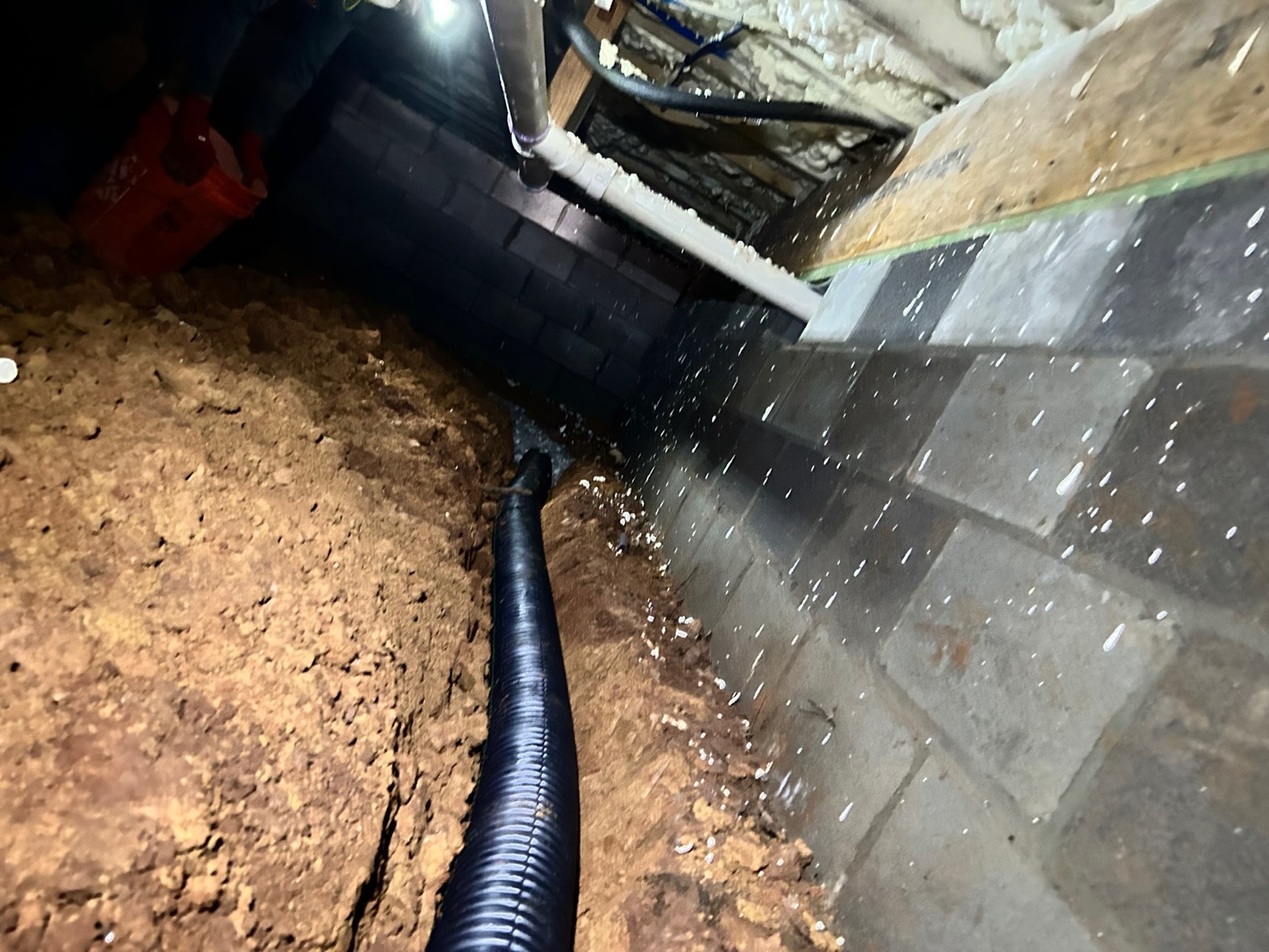 Perforated drain pipe carrying water out through a crawlspace block wall — Crawl Daddy interior drainage install in Metro Atlanta